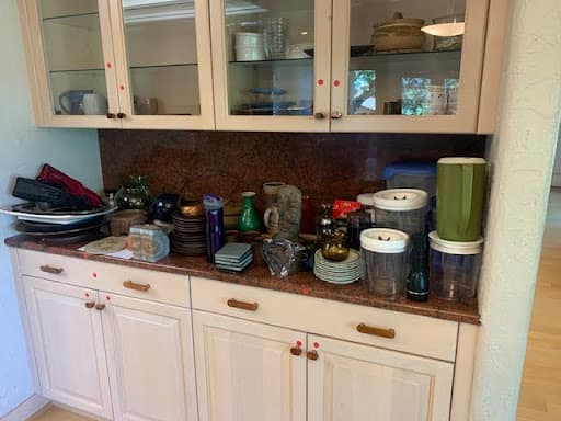Photo shows kitchen cabinets with dishes and other kitchen items stacked on the countertop.