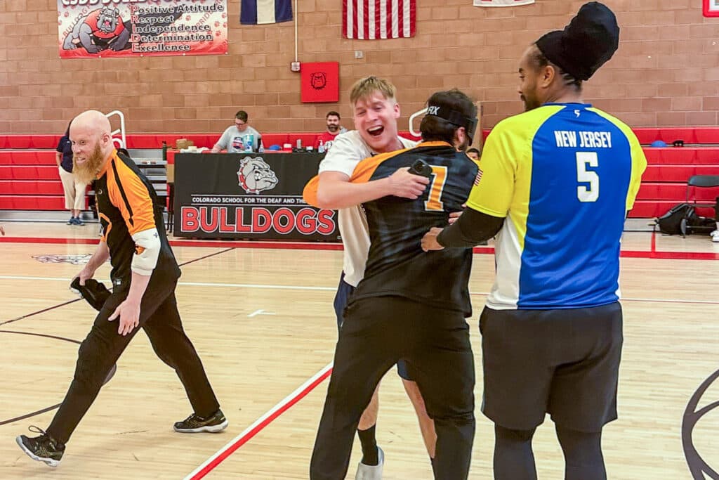 Two men embrace on a goalball court as two other players look on.