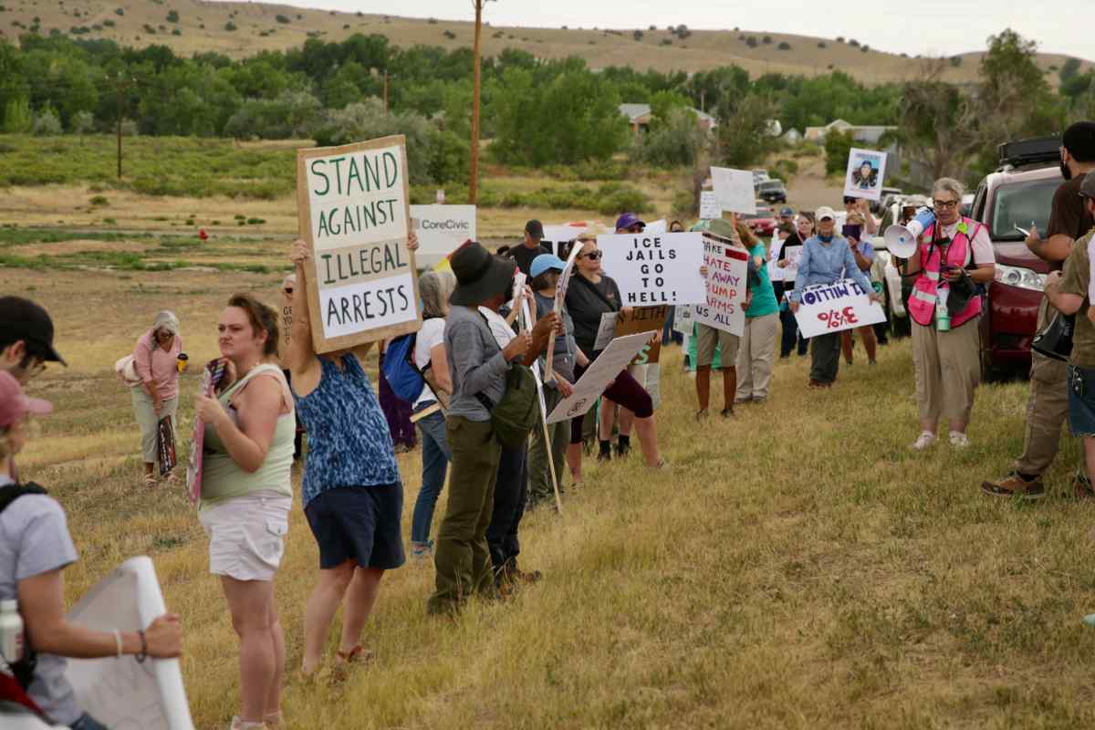 A group of about 100 people line a hillside holding signs protesting the possible opening of an immigration detention center.