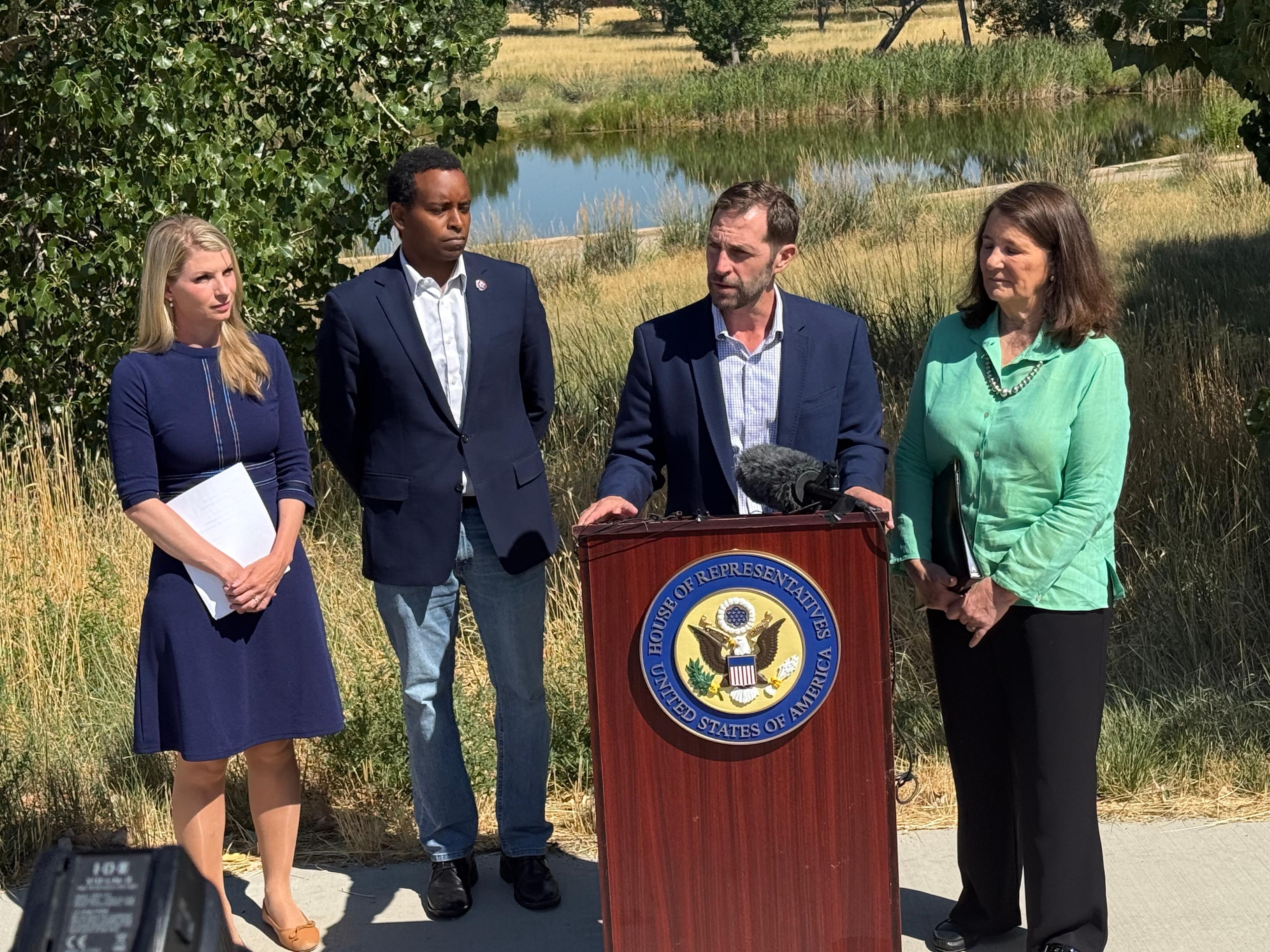 Four people gathered behind a lectern featuring the logo of the U.S. House of Representatives