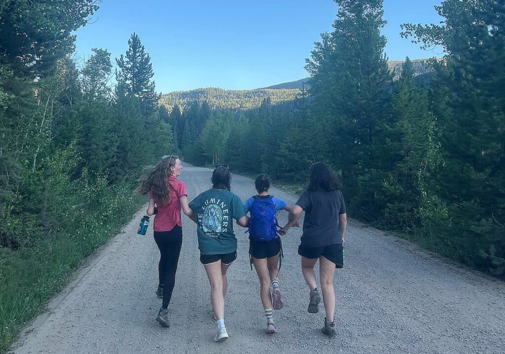 Four high schoolers run up a gravel road in a wilderness area.