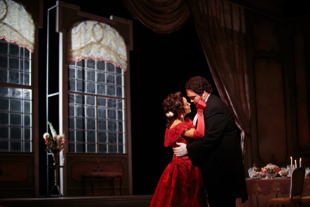 A man and woman in formalwear embrace, faces close together.