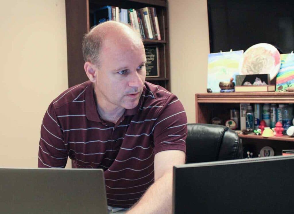 Man in a maroon striped polo in a home office looking at computer screens