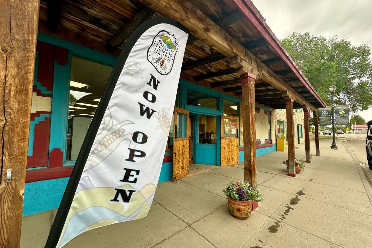 A sign reading "Now Open" stands outside the San Luis Peoples Market.