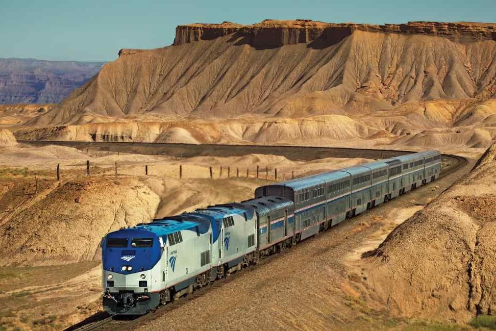 a blue and silver amtrak train with a desert background