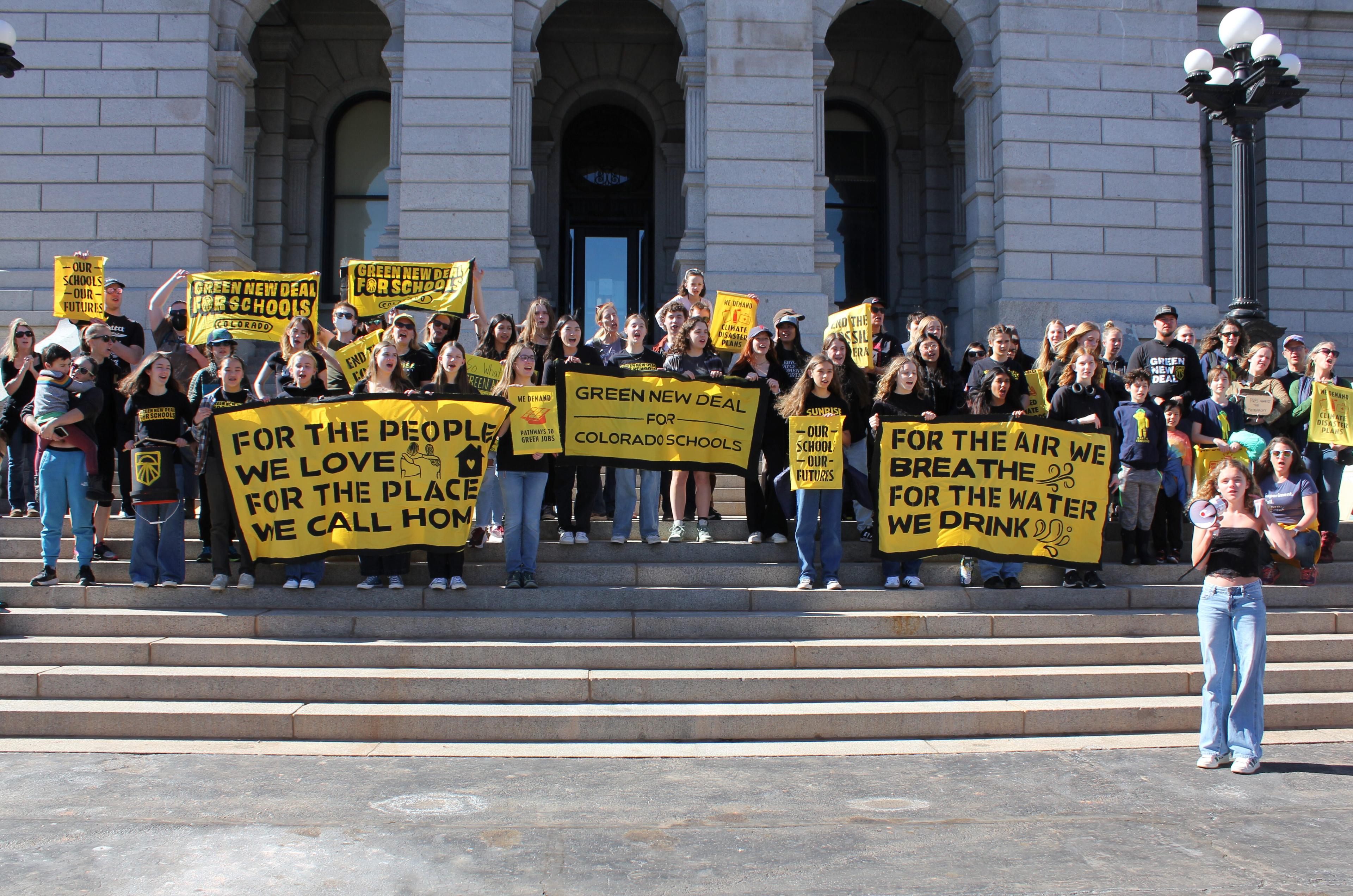 A group of about three dozen high school students stand on the steps of the Colorado Capital holding signs and banners that say Green New Deal for Schools and Our Schools Our Futures.
