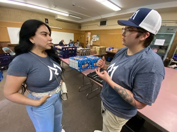 Two people in dark t-shirts speak in a church cafeteria during a recent health fair.