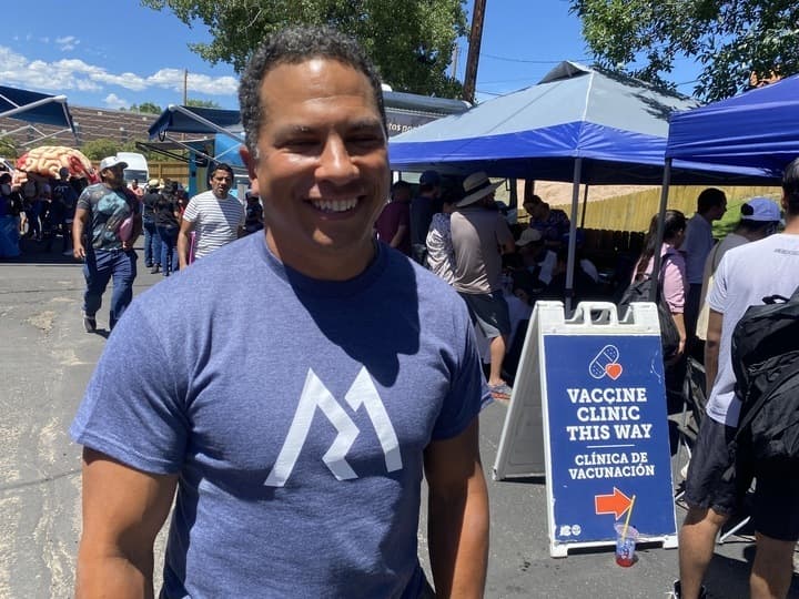 Man in dark blue t-shirt stands before a vaccine clinic sign at a Latino health fair in Denver.