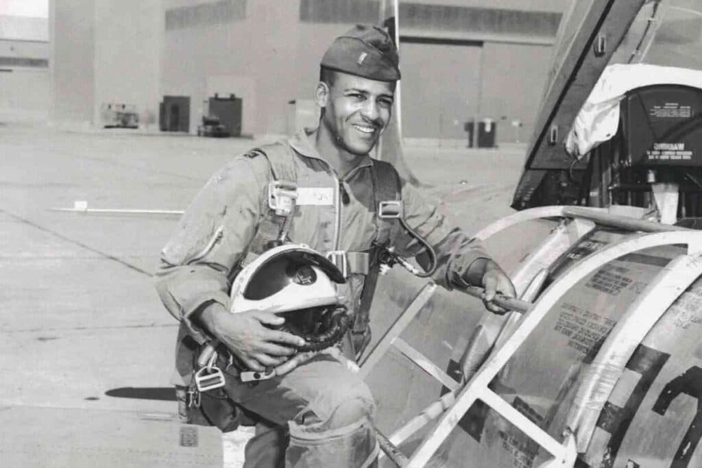 A black and white photo of a man in an Air Force uniform in the process of climbing into a plane with helmet in hand