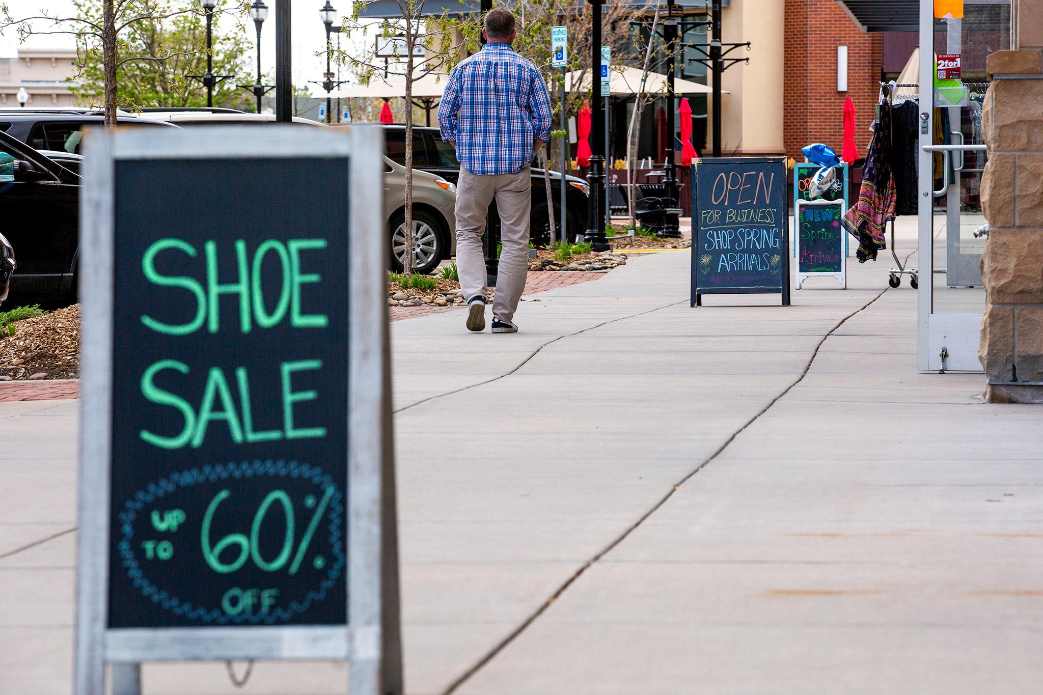 A person walking down the sidewalk away from the camera in front of shops