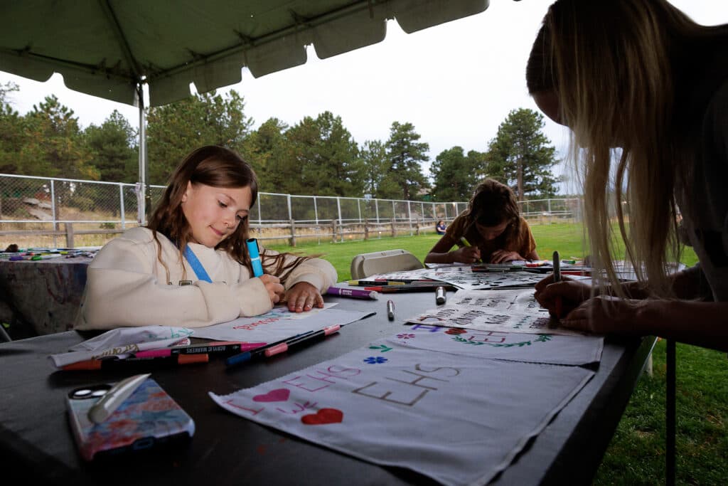 Ruthie Fitzpatrick makes a sign with her friends at one of the art tents at a vigil