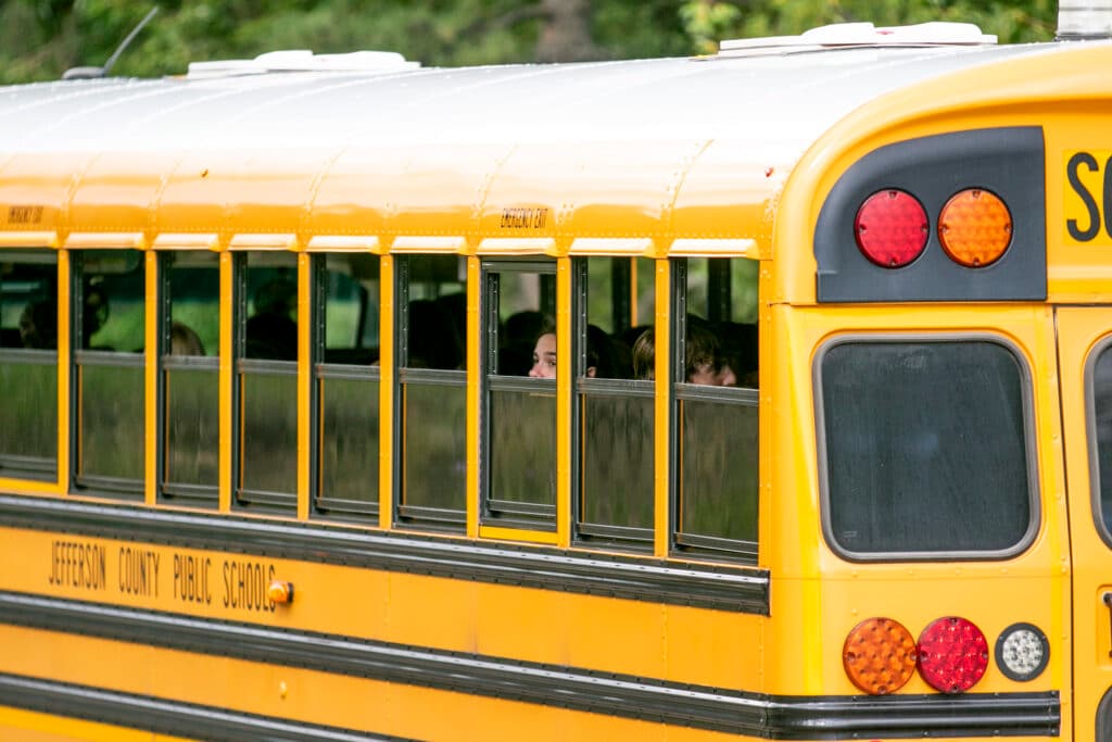 Teens look out the windows of a yellow school bus.