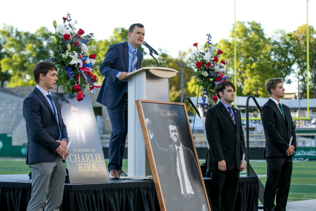 A man wearing a blue suit and a blue tie is speaking into a microphone.