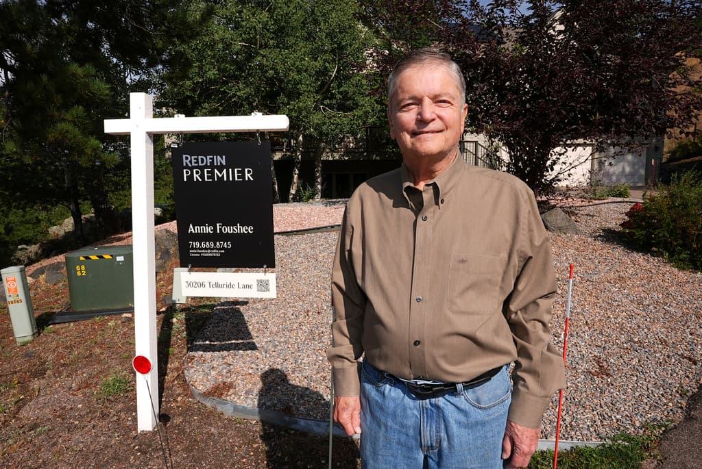 A man stands in front of a home for sale sign