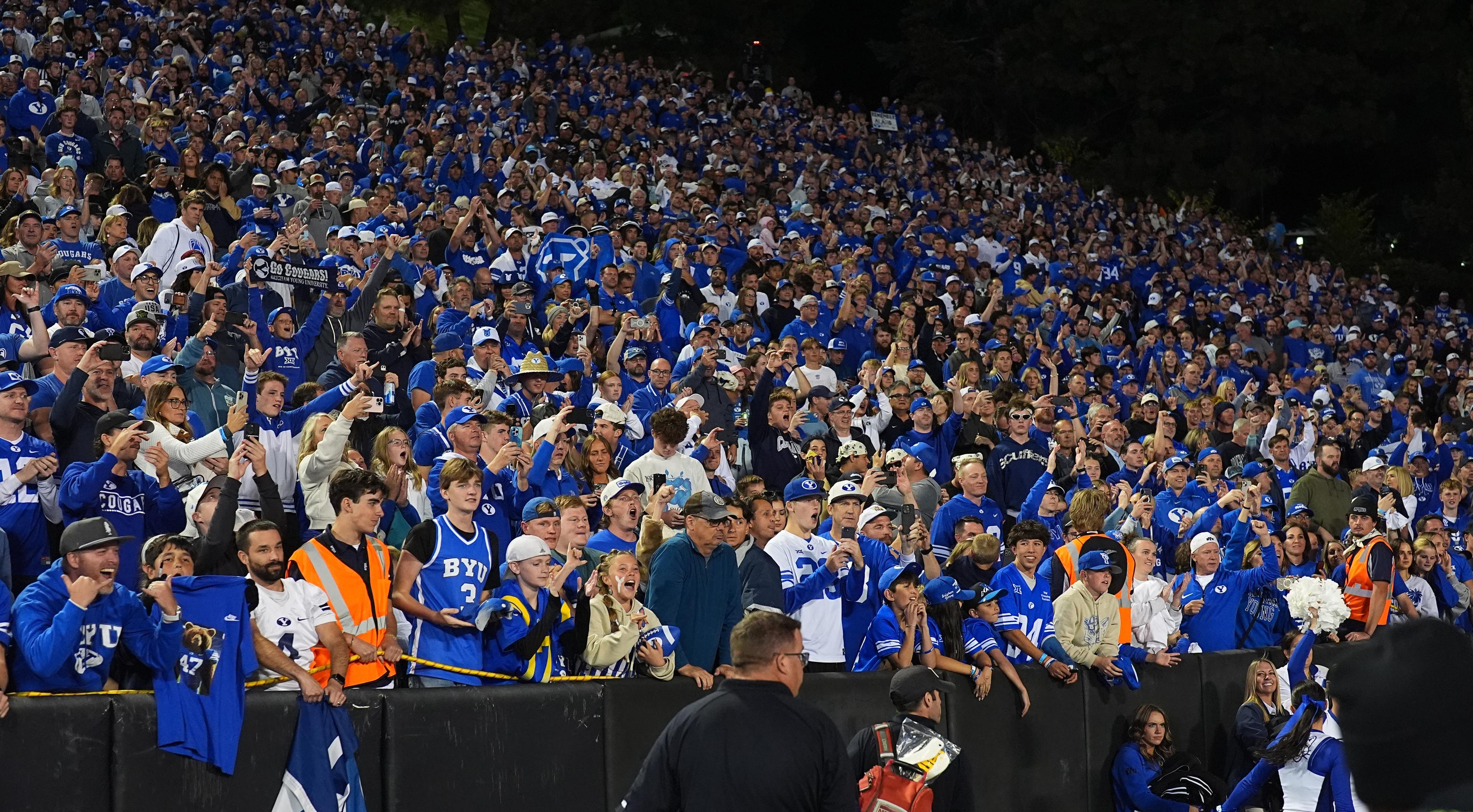 A large crowd of people is gathered in a stadium, watching a game. They are standing and sitting in various positions, with some holding up their cell phones to capture the moment.