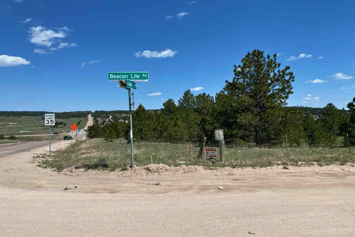 Tree filled lot at intersection with street sign for Beacon Lite Road.