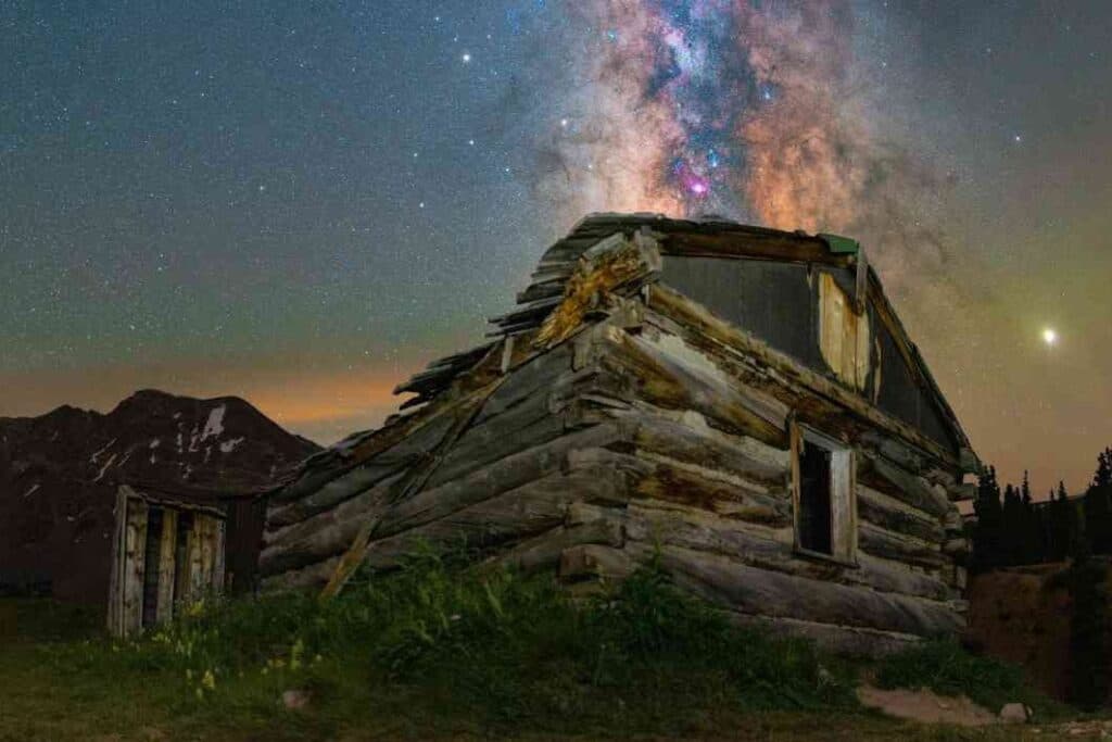 The Milky Way in the night sky over a log cabin.