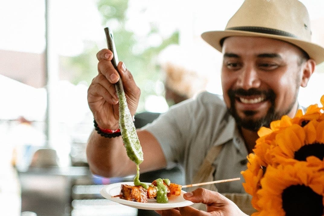 A man spoons a green sauce onto a kabob.