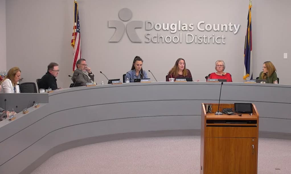 A screen picture of seven member of the Douglas County School District board, each sitting behind a microphone on a curved desk.