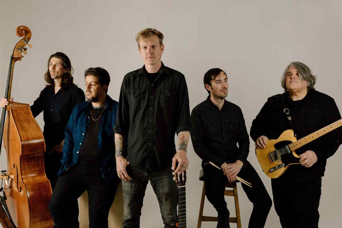 Five people wearing black. On the left one person is holding a bass violin. On the right, the person standing has a guitar over his shoulder. This is an image of the band, "Gasoline Lollipops."