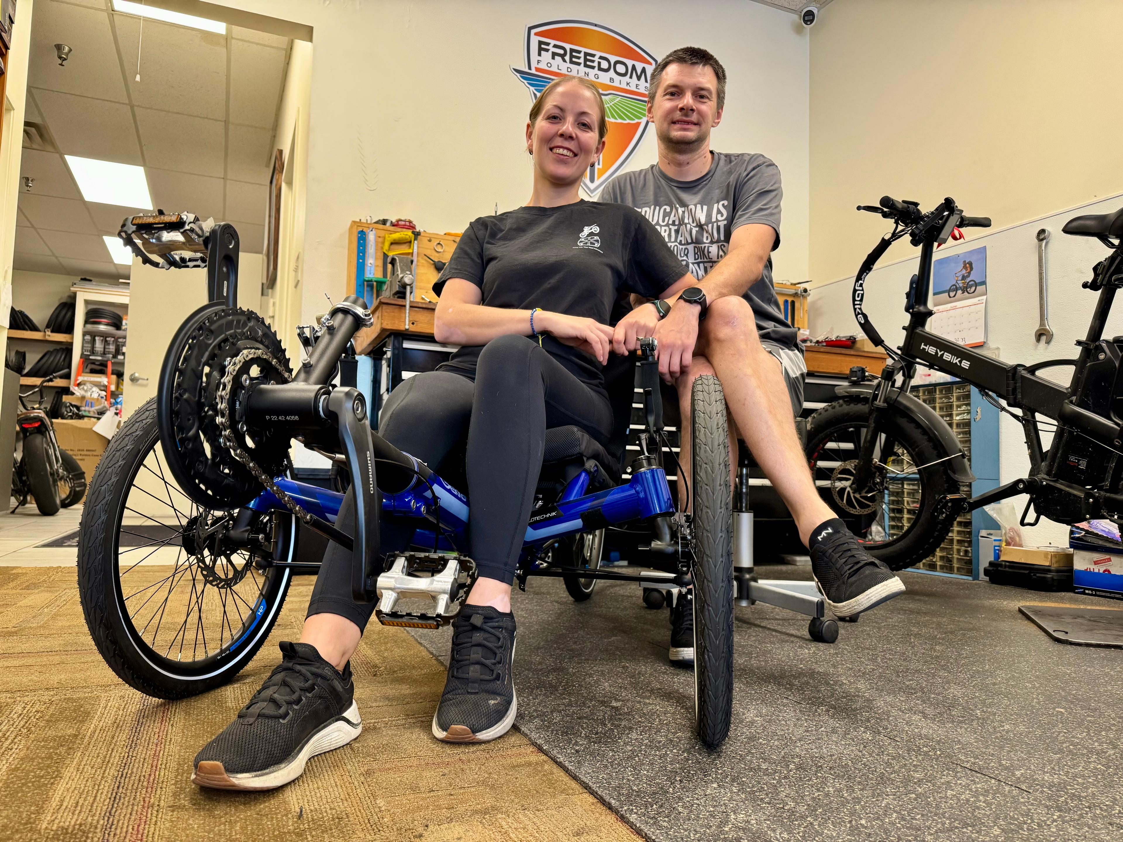 Smiling couple sits in a recumbent bike at their store.