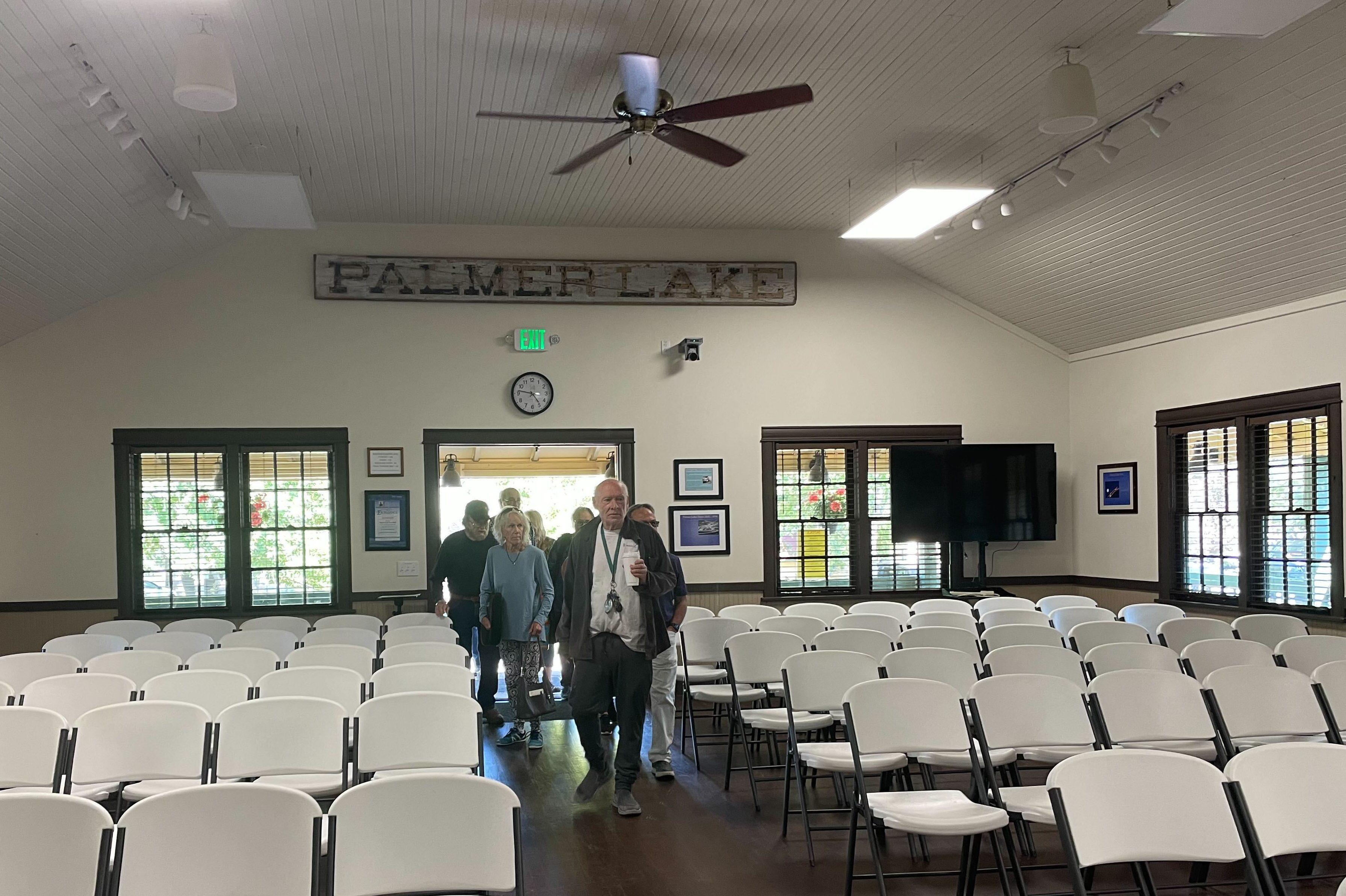 a large hall full of folding chairs with a crowd of people entering through a door in the far wall