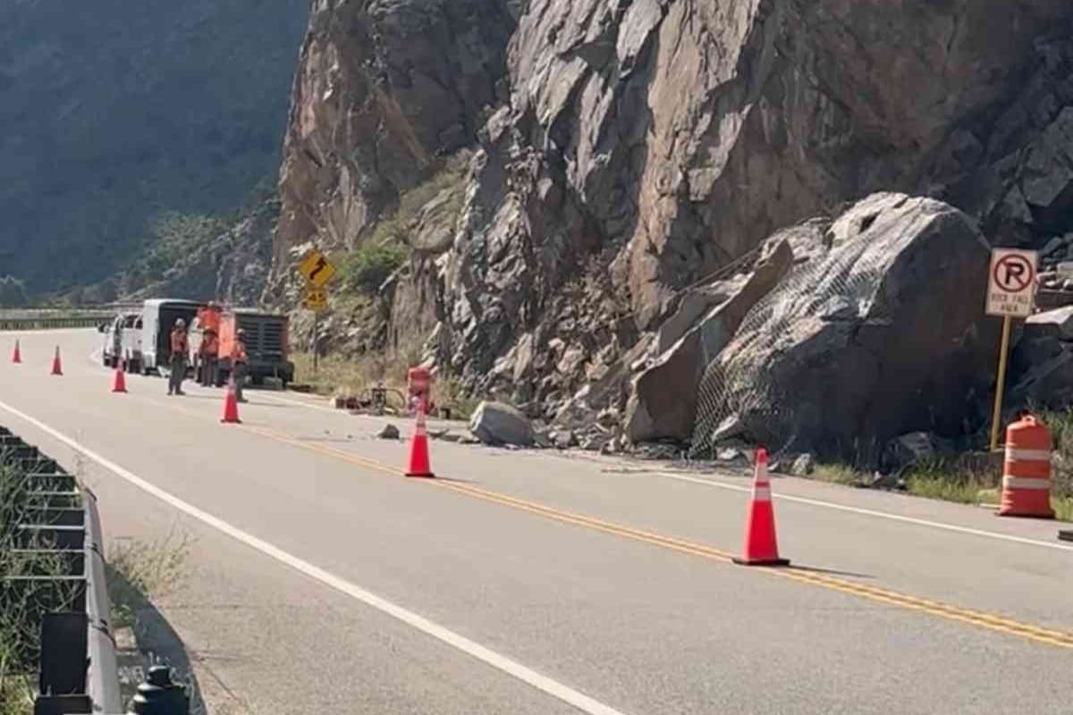 road crew works near a cliff face with orange cones set up