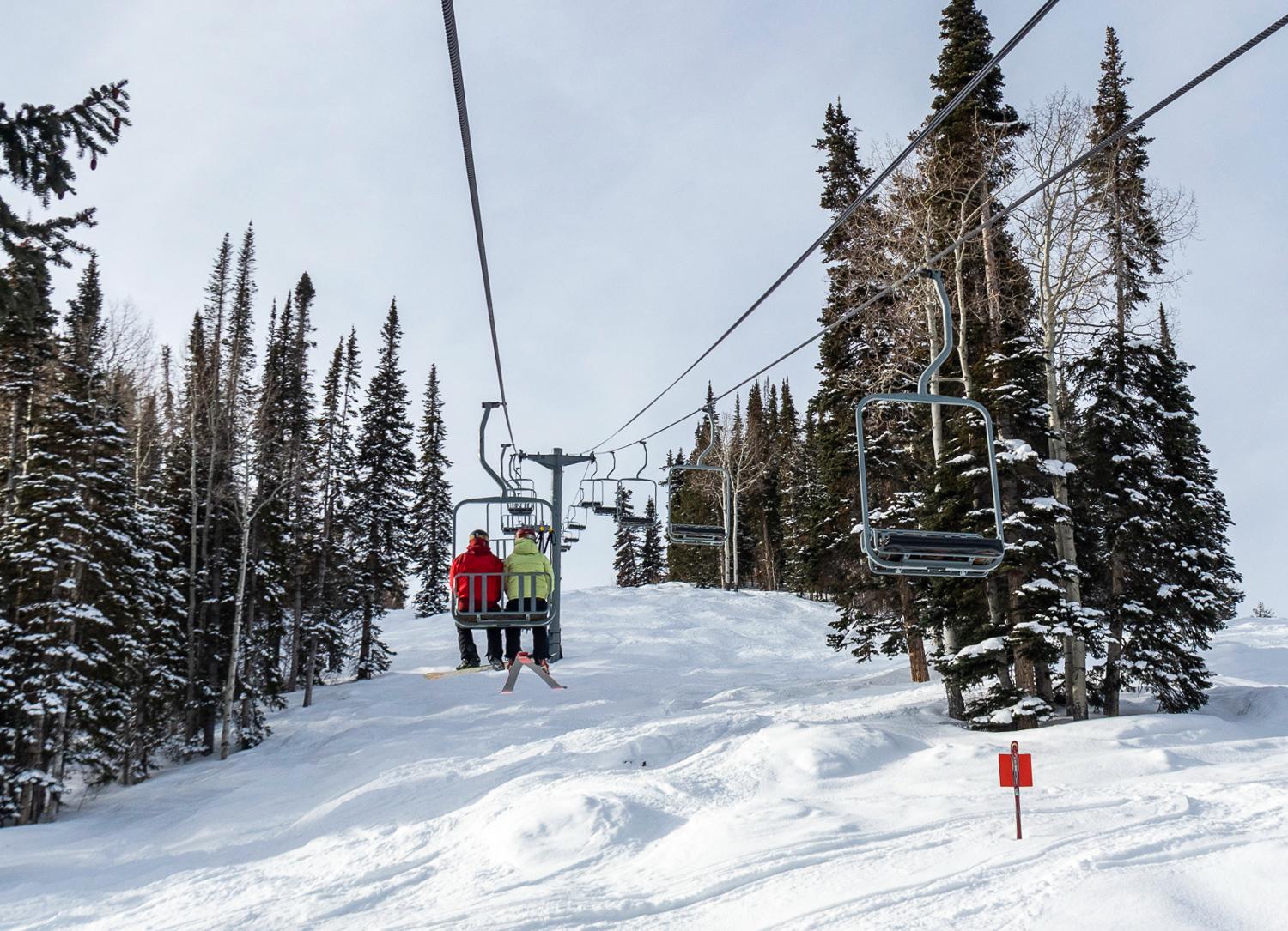 Two skiers are seen from behind riding an old, two-person chairlift above a bumped ski run at Powderhorn Mountain Resort.