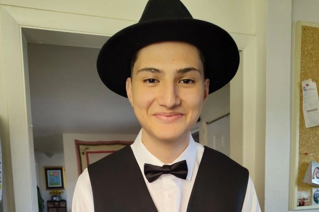A young man in a black hat white dress shirt black vest and bowtie