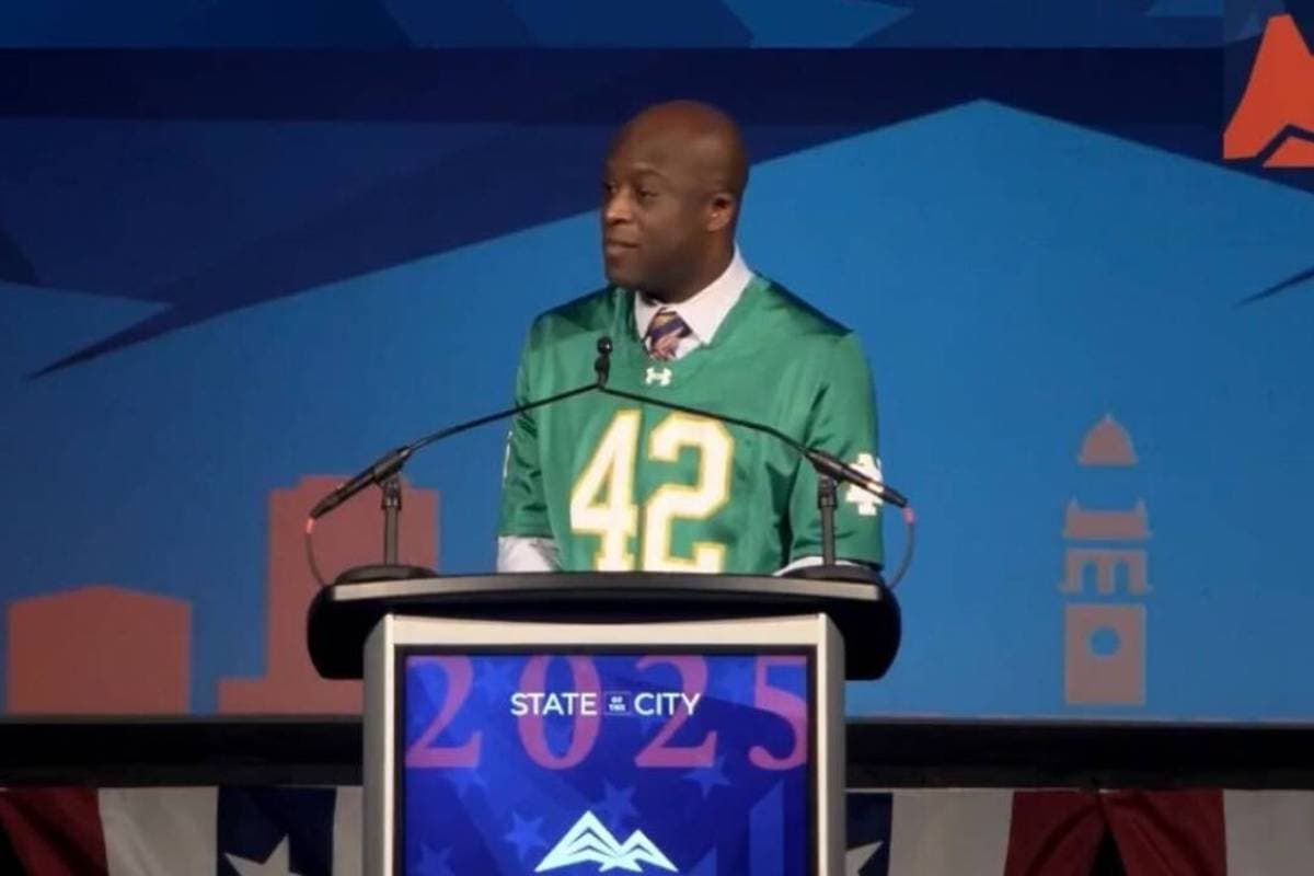 A man in a football jersey speaks at a podium