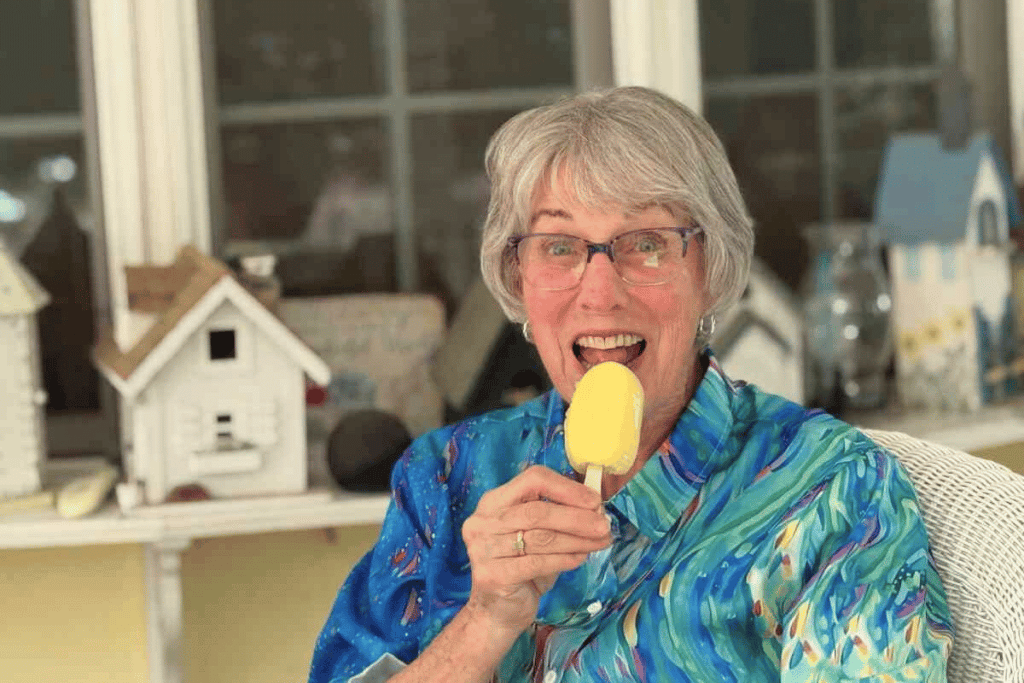 A woman smiles at the camera holding a yellow popsicle