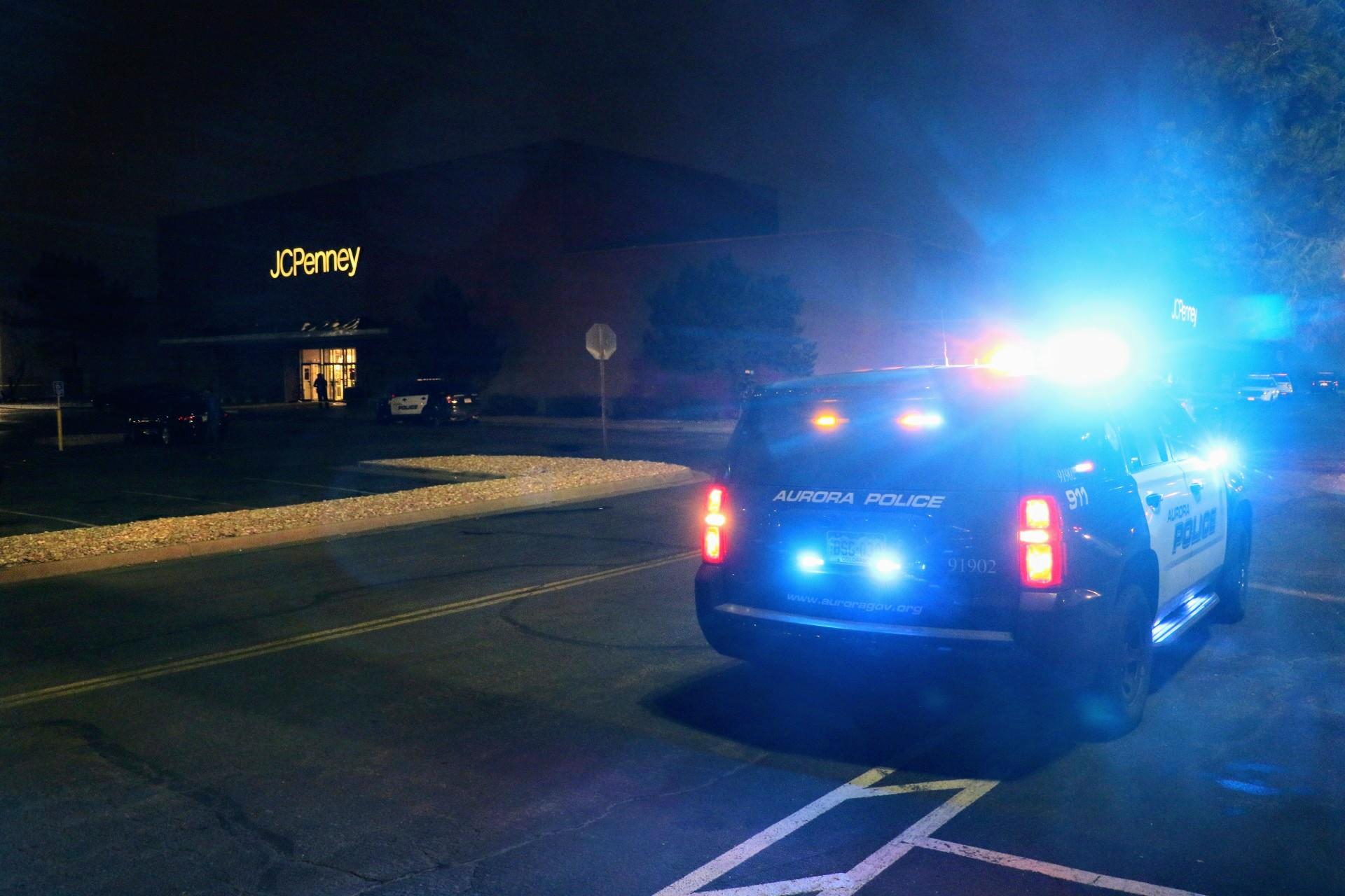 An Aurora Police Vehicle with lights on, parked in front of a JCPenney during at night.