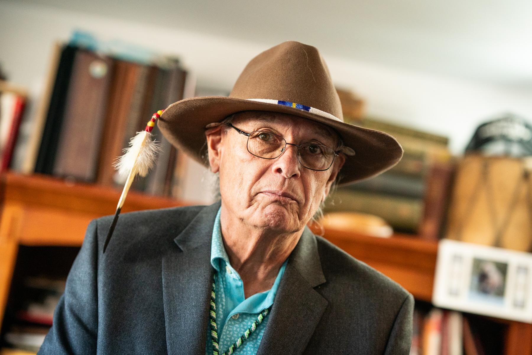 Rick Williams in a broad western hat, beaded hat band and feather quill, in a turquois shirt and grey suit jacket.