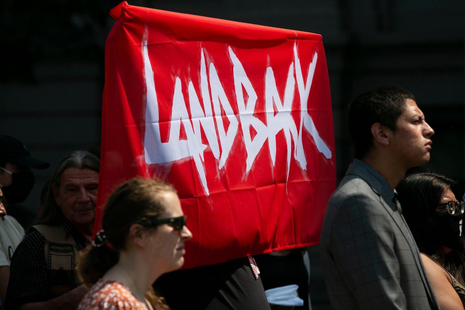 Land Back movement supporters hold up a red and white banner