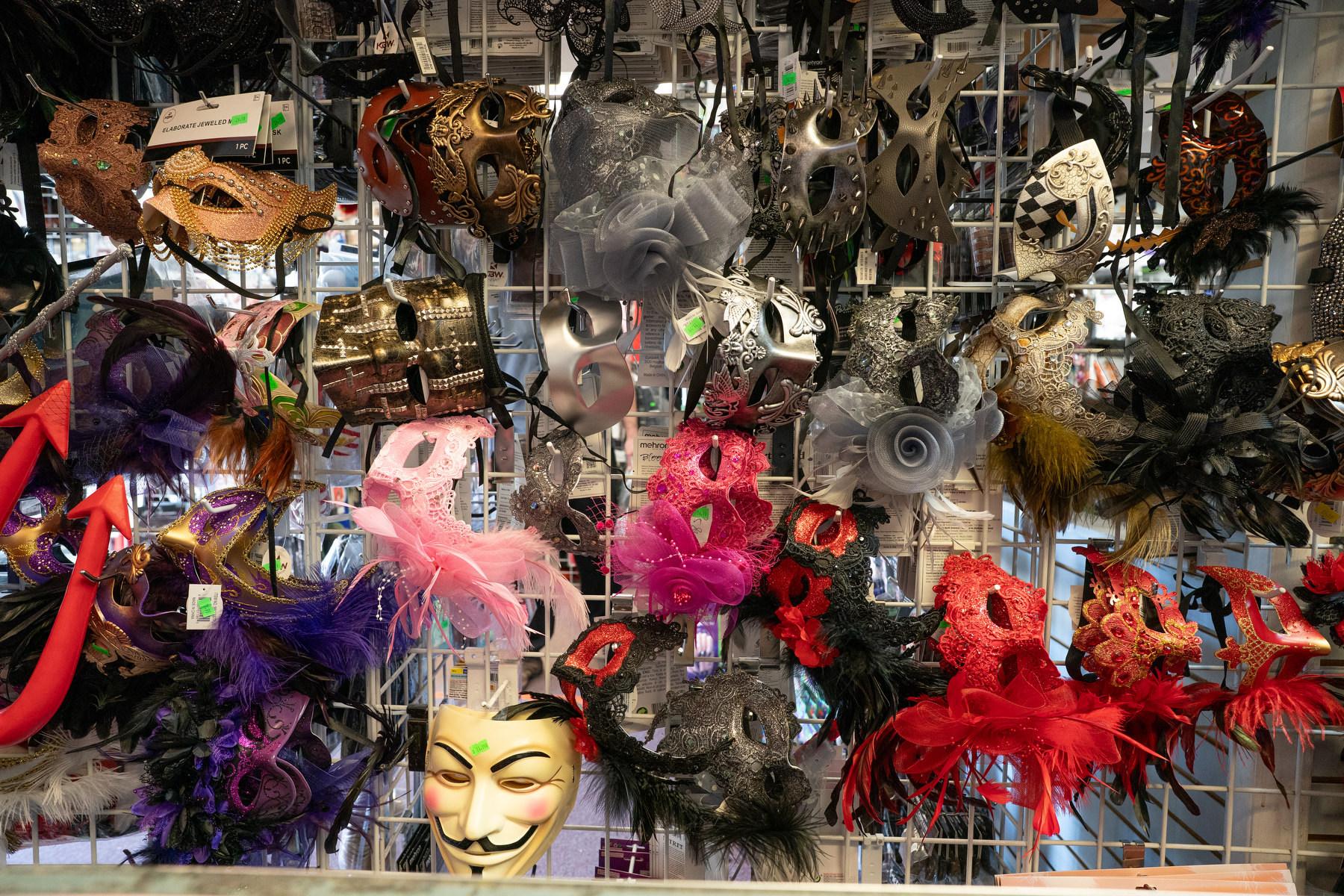 A display of various masks, including a mask with a hood and a mask with a face painted on it, are arranged on a rack.