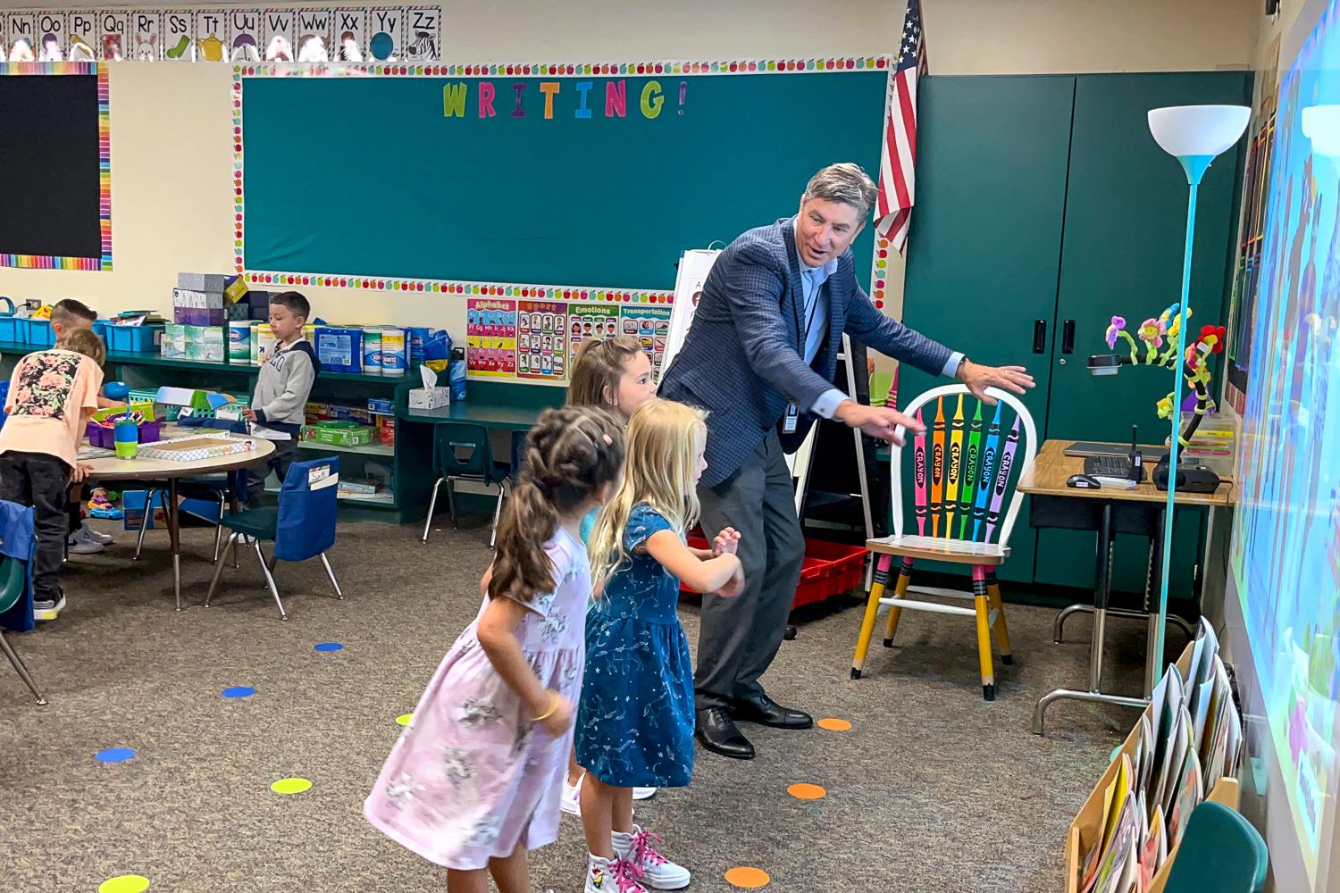 A man dances with children in a classroom.