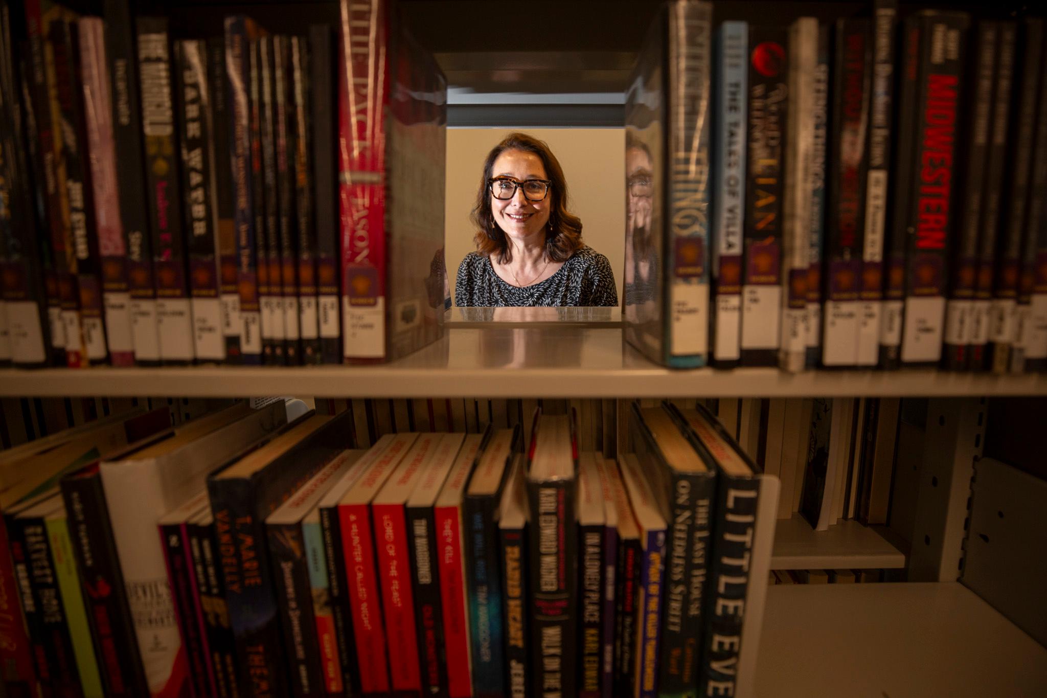A woman's face is seen looking through shelves of books