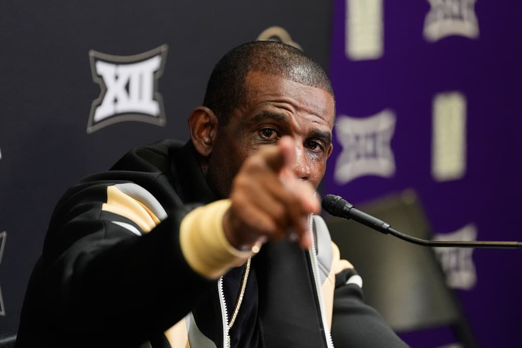 Coach deion points at camera from press podium.