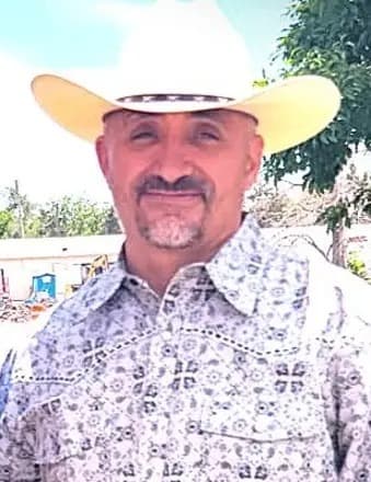A man poses for the camera wearing a button shirt and cowboy hat