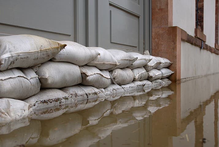 Sandbags lined up along the edge of a doorway, with standing brown water next to it.