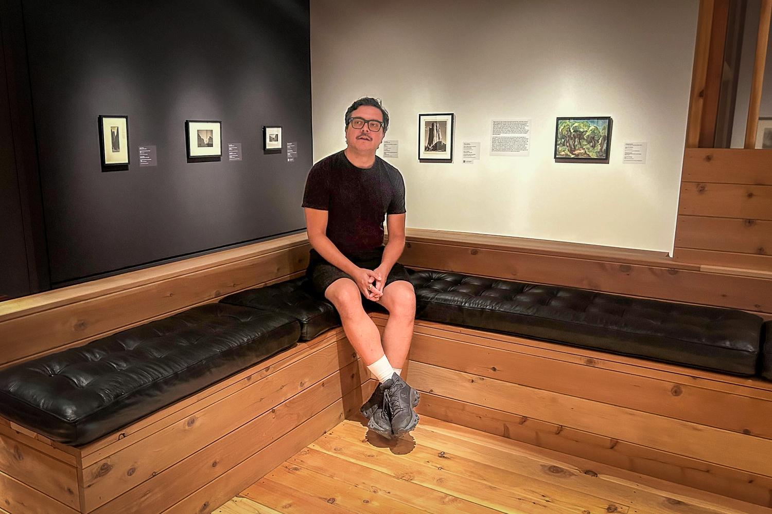 A person in a black shirt and shorts sits on a black corner booth
