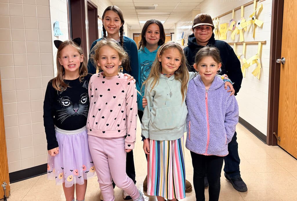 A group of children posing for a picture, with some wearing pink and purple shirts. The children are smiling and enjoying the moment.