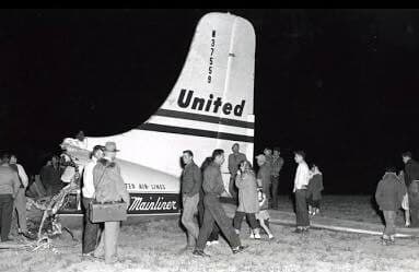 In a black and white photograph, a crowd is seen around the tail section of United flight 629, which was bombed shortly after taking off from Denver.