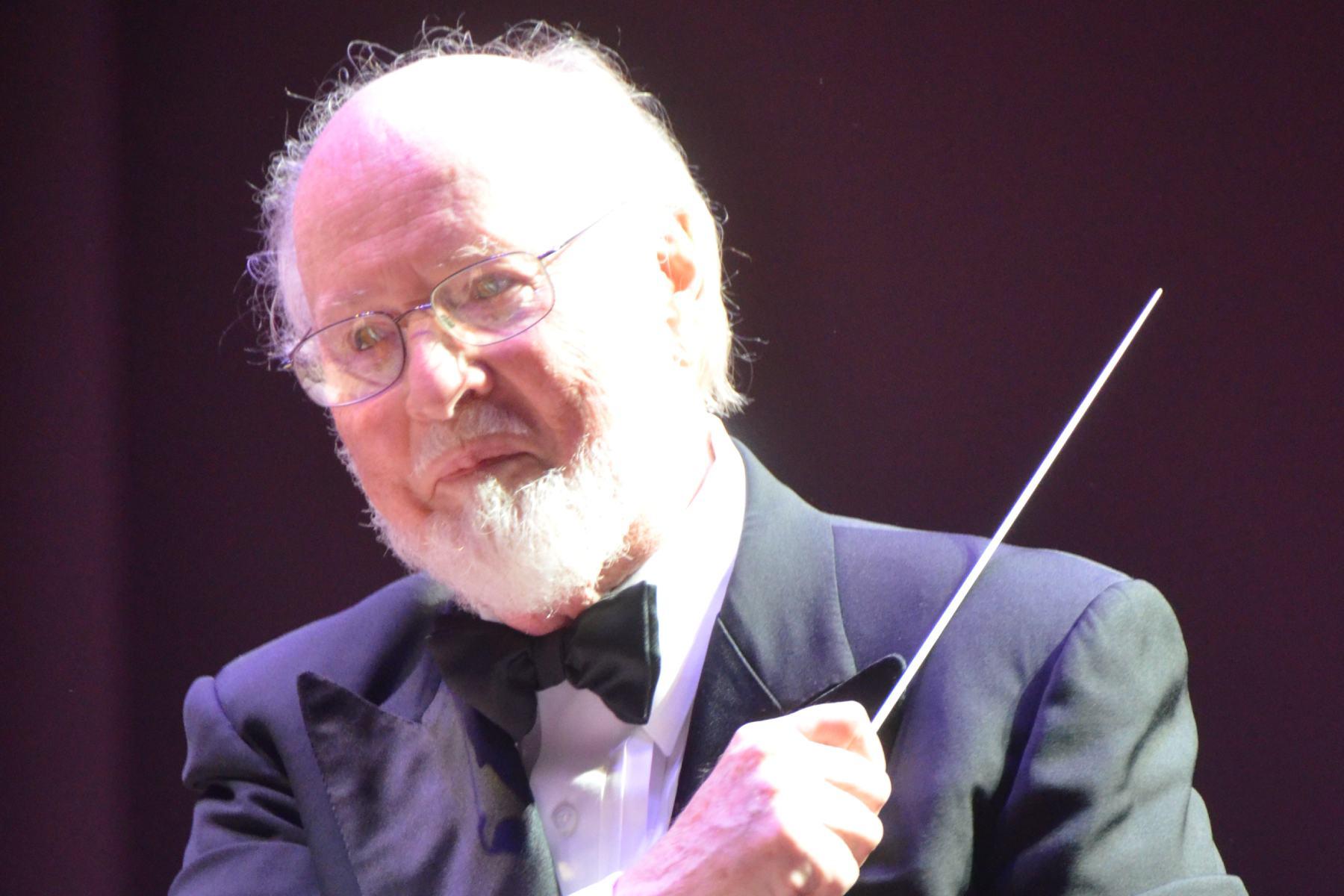 Man with gray hair and gray beard in jacket and bowtie holding a conductor's baton.