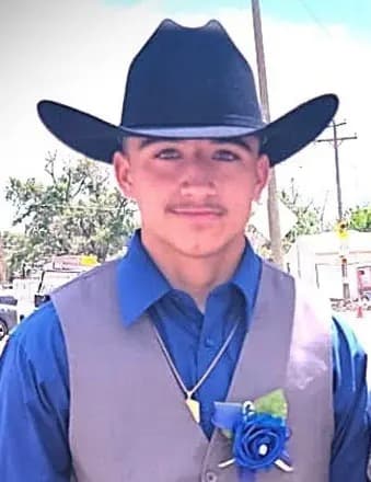 A boy wearing a cowboy hat and a blue shirt with a flower pinned to his vest.