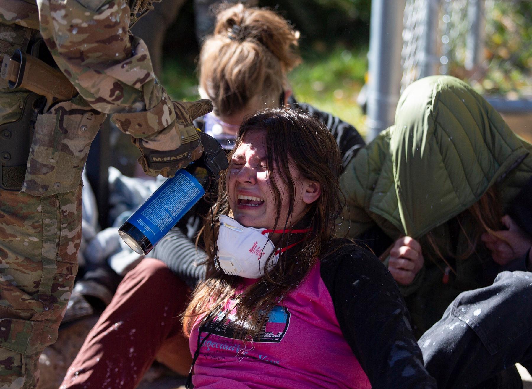 A group of people are gathered around a woman who is wearing a gas mask. The woman is sitting on the ground, and the others are standing around her.