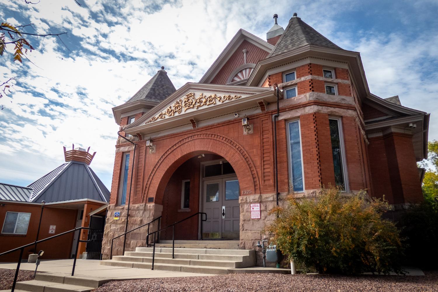 Historic red brick building with complex roof and architecture including a large arch entryway with decorative work. Next door is a smaller more modern building