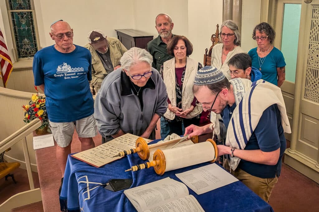 People gather around blue velvet covered lectern where a scroll is unrolled and the people are engaged in the content.