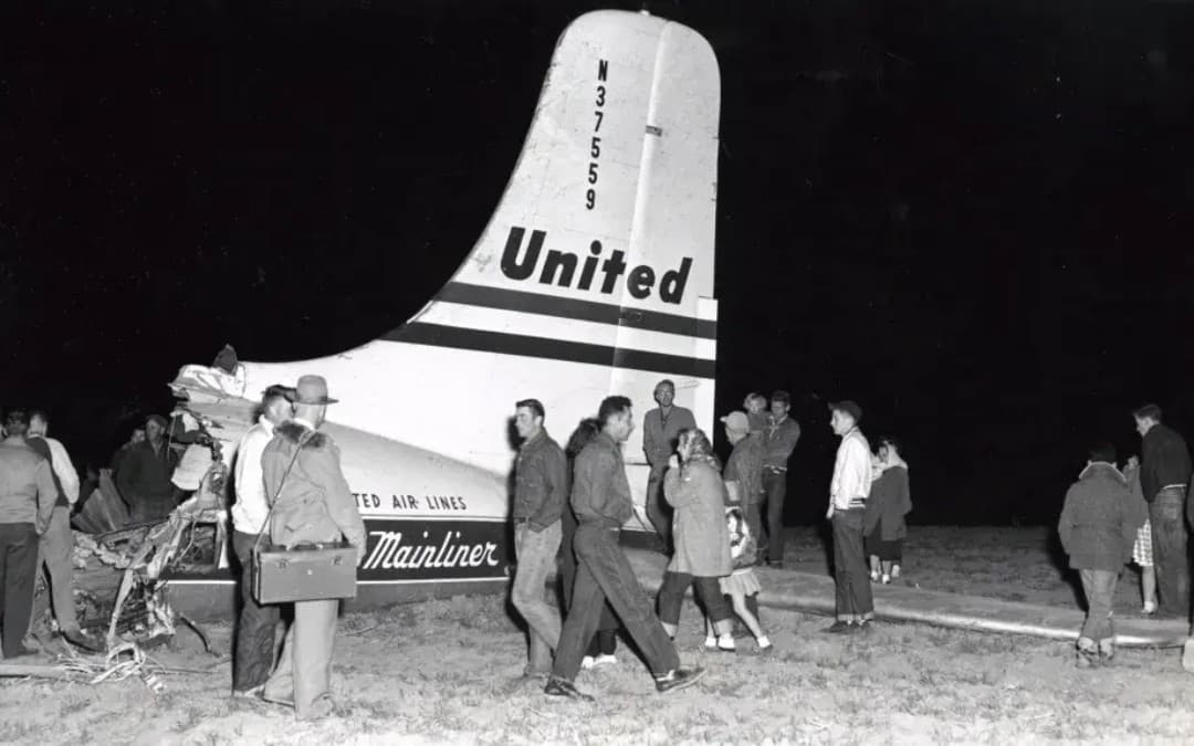 black and white photo of a crowd standing around a plane crash