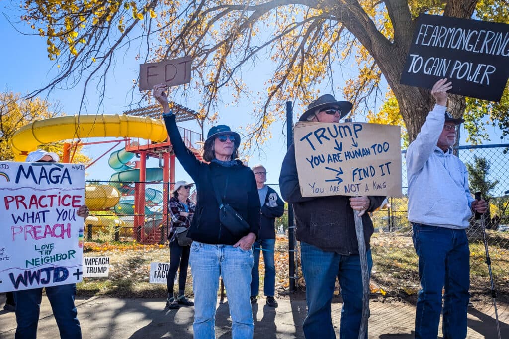 A group of people are gathered near a park, holding signs and protesting. They are standing on a sidewalk